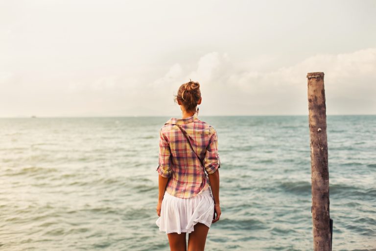 Back of woman in a white skirt looking at the sea.