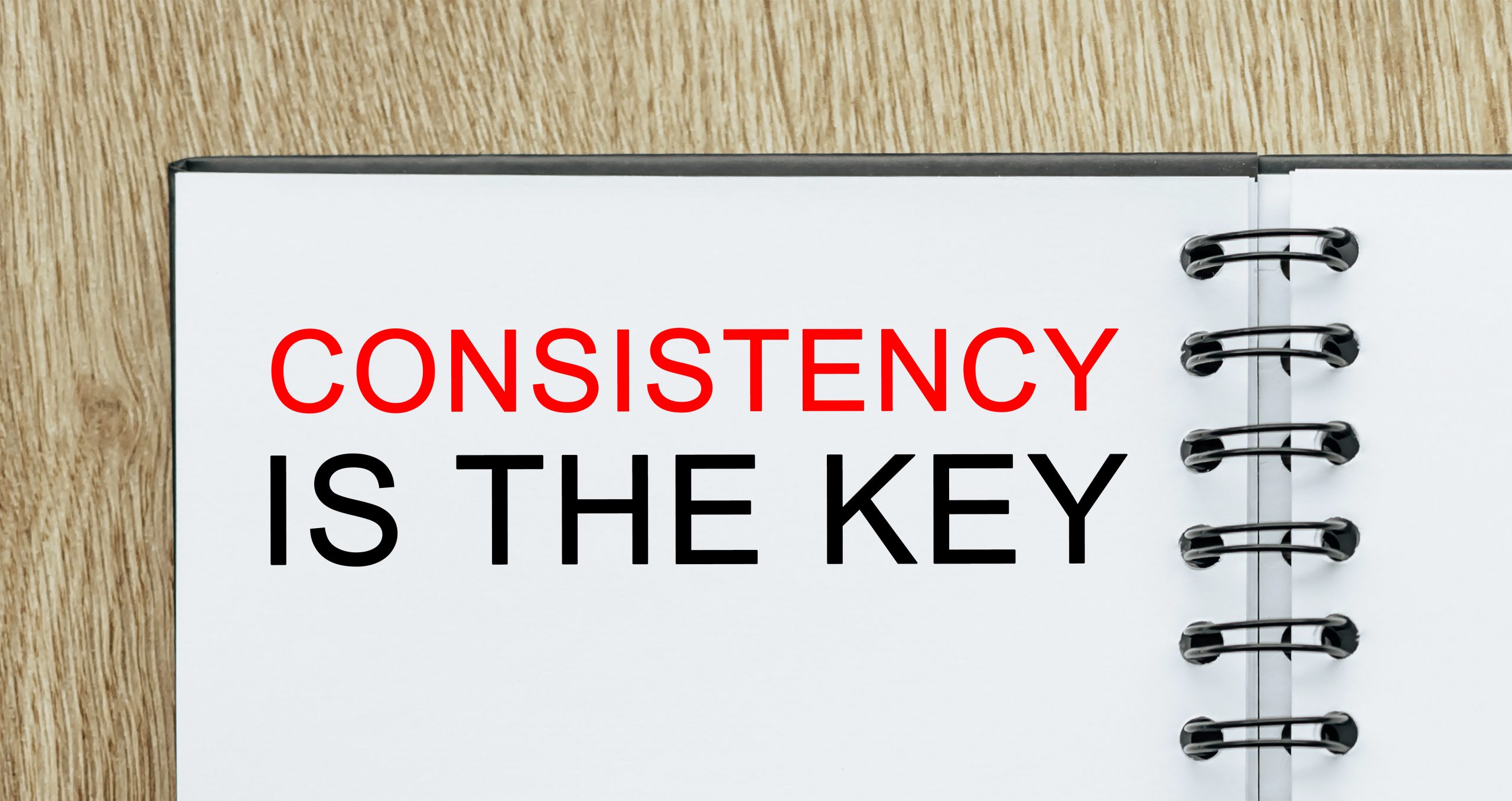 'Consistency is the key' in a notebook on a wooden desk