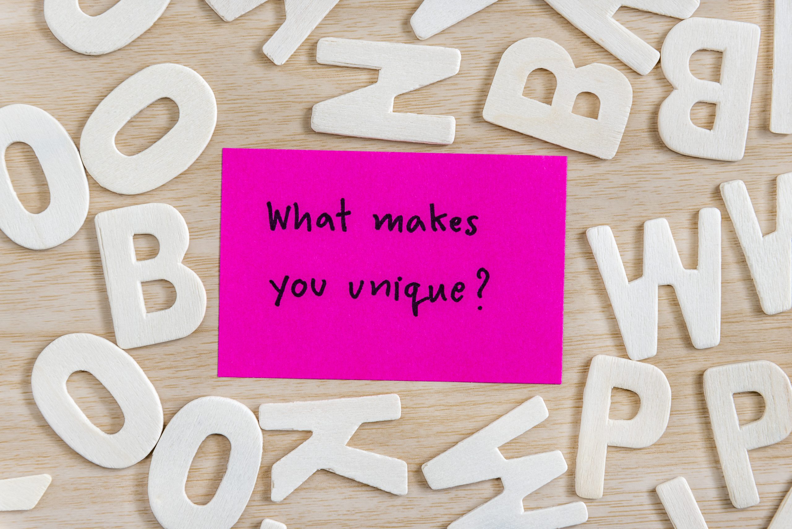 'What makes you unique?' on a pink sticky note surrounded by letters on a wooden desk