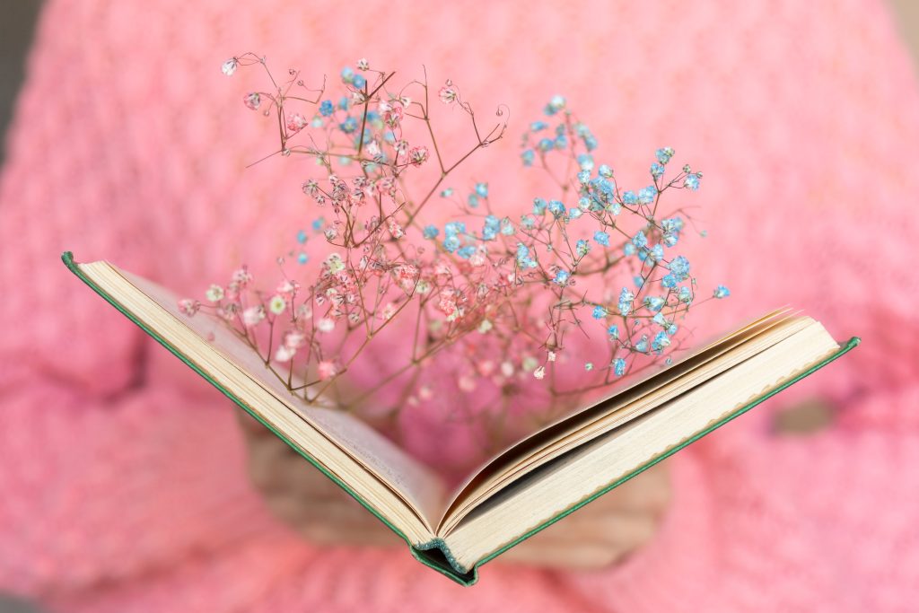 Woman in a pink jumper holding an open book with blue flowers.
