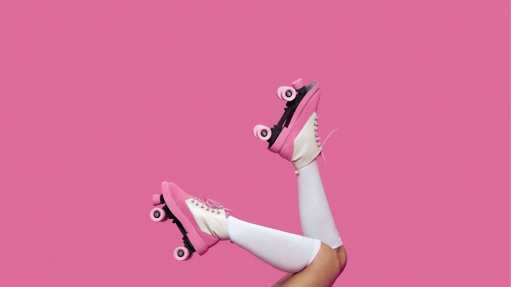 A pair of female legs pointing upwards with knee-high white socks and pink roller skates.