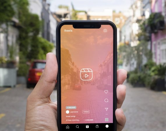 Hand holding phone with Instagram Reels screen in front of a street