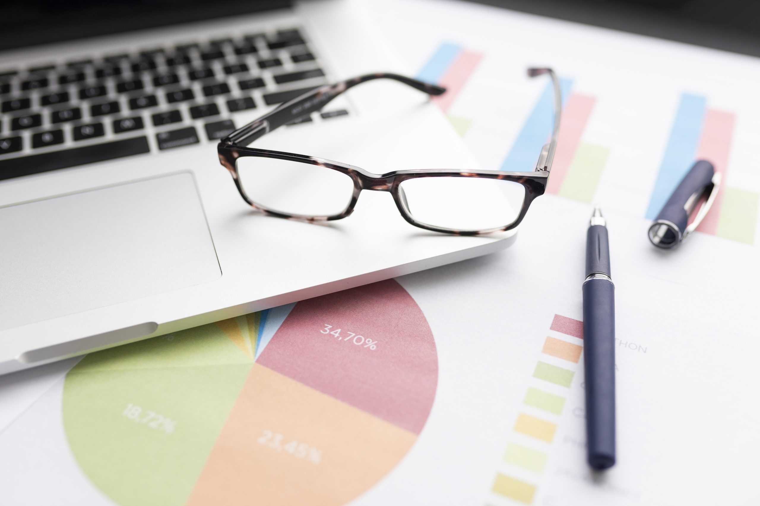 Laptop with glasses on, surrounded by data and charts on paper