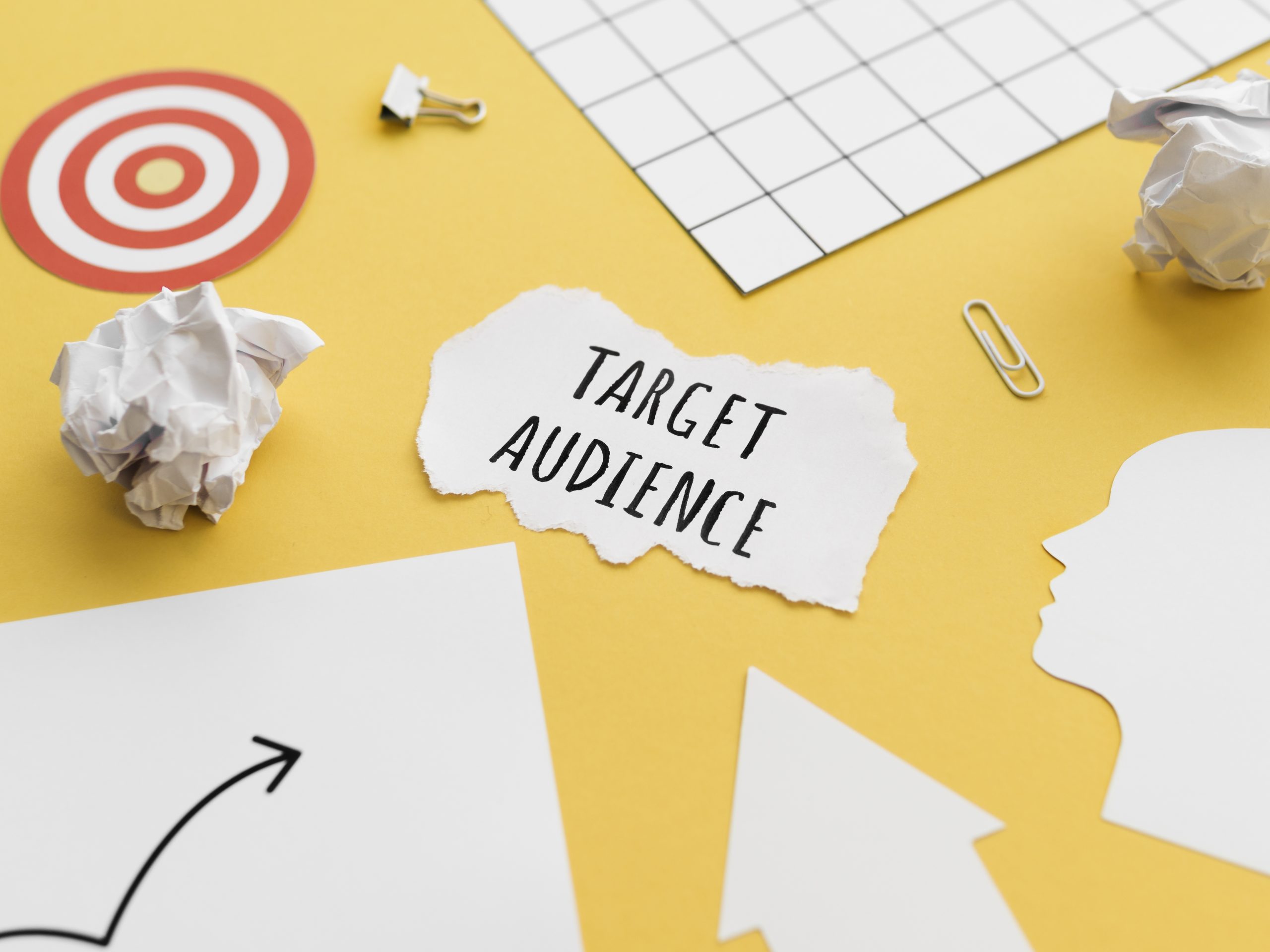 'Target Audience' written on piece of paper surrounded by bits of paper and a paper clip on a yellow surface