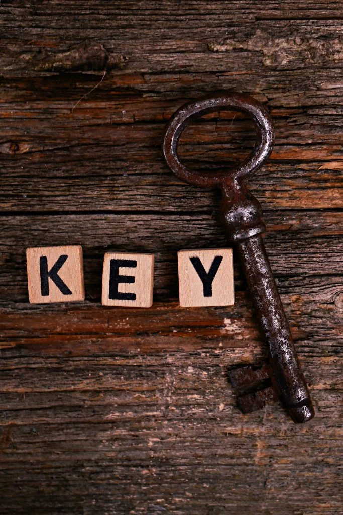 Old, rustic key on a table beside the word 'key' spelt out with scrabble letter tiles
