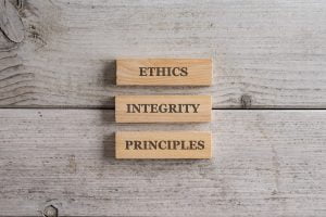 Words Ethics, Integrity and Principles written on three stacked wooden blocks placed over white wooden background.
